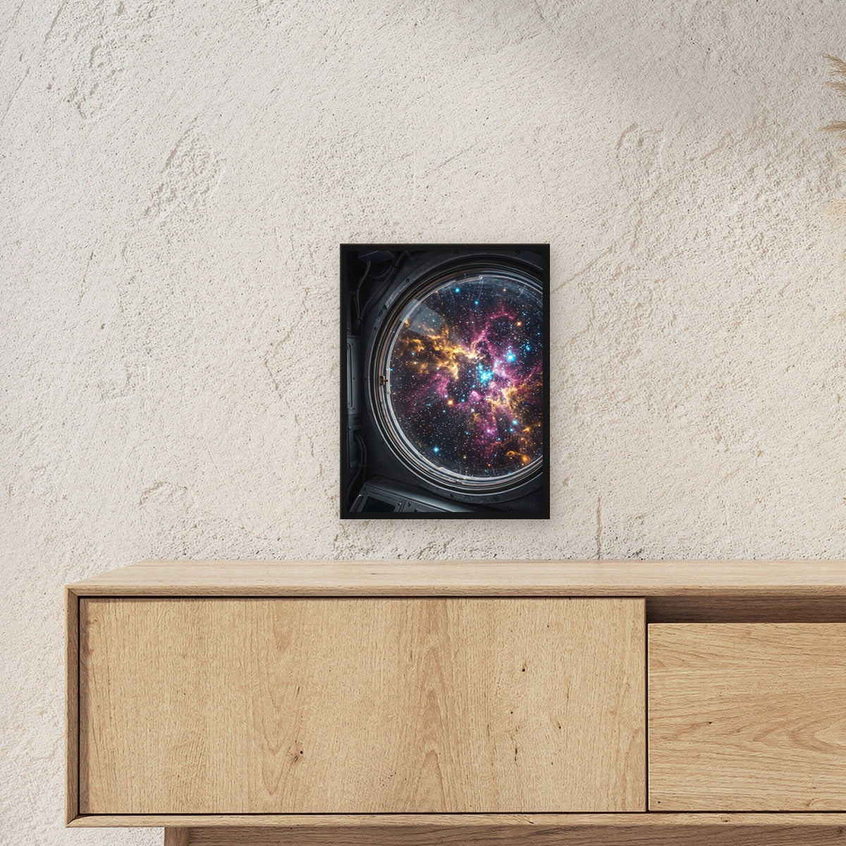 Blick durchs Bullauge – Rundes Bullauge mit Sternennebel in Pink und Gold, im schwarzen Holzrahmen, über einem Sideboard