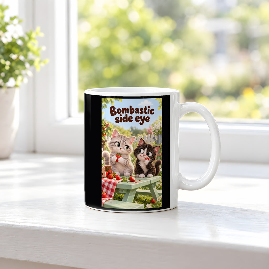 Zwei Kätzchen mit Erdbeeren auf einer Gartenbank werfen sich einen Seitenblick zu. Spruch: Bombastic side eye – weiße Tasse, Ansicht am Fenster.