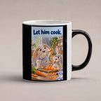 Zwei Kaninchen spielen in einer hellen Küche mit langen Möhrenstreifen; eines trägt eine karierte Schürze. Spruch: Let him cook. – Black Edition mit Wärmeeffekt, Studioansicht.