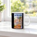 Zwei Kaninchen spielen in einer hellen Küche mit langen Möhrenstreifen; eines trägt eine karierte Schürze. Spruch: Let him cook. – weiße Tasse, Ansicht am Fenster.