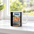 Ein schläfriger Hamster kuschelt in einer grünen Tasse zwischen Blaubeeren und einer kleinen Decke. Spruch: Eepy. – weiße Tasse, Ansicht am Fenster.