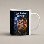 Eine müde Eule mit violetter Schlafmütze gähnt vor einer Baumhöhle unter dem Mond und hält ein kleines Blätterbündel. Spruch: Ich habe fertig! – weiße Tasse, Studioansicht.