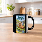 Ein entspanntes Capybara mit einem Blatt auf dem Kopf liegt auf einem großen Seerosenblatt; eine kleine Schildkröte schwimmt daneben. Spruch: Just a chill guy. – Tasse innen schwarz, Küchenansicht.