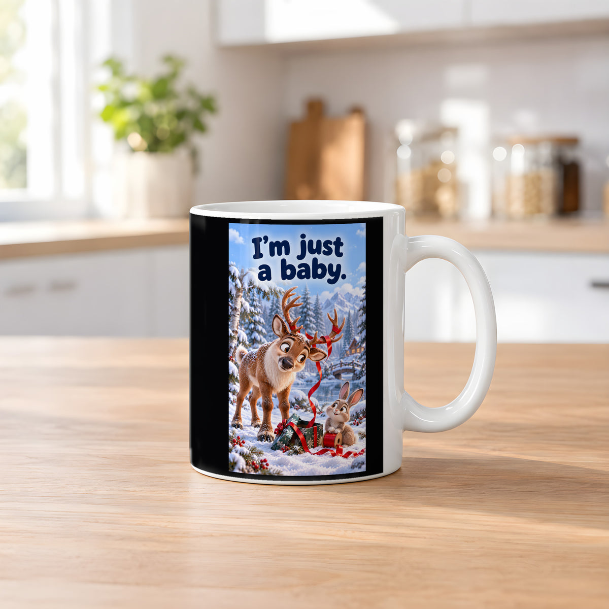 Ein Rentier mit rotem Geschenkband im Geweih blickt zu einem Kaninchen mit einer Bandrolle neben einem Geschenk im Schnee. Spruch: I'm just a baby. – weiße Tasse, Küchenansicht.