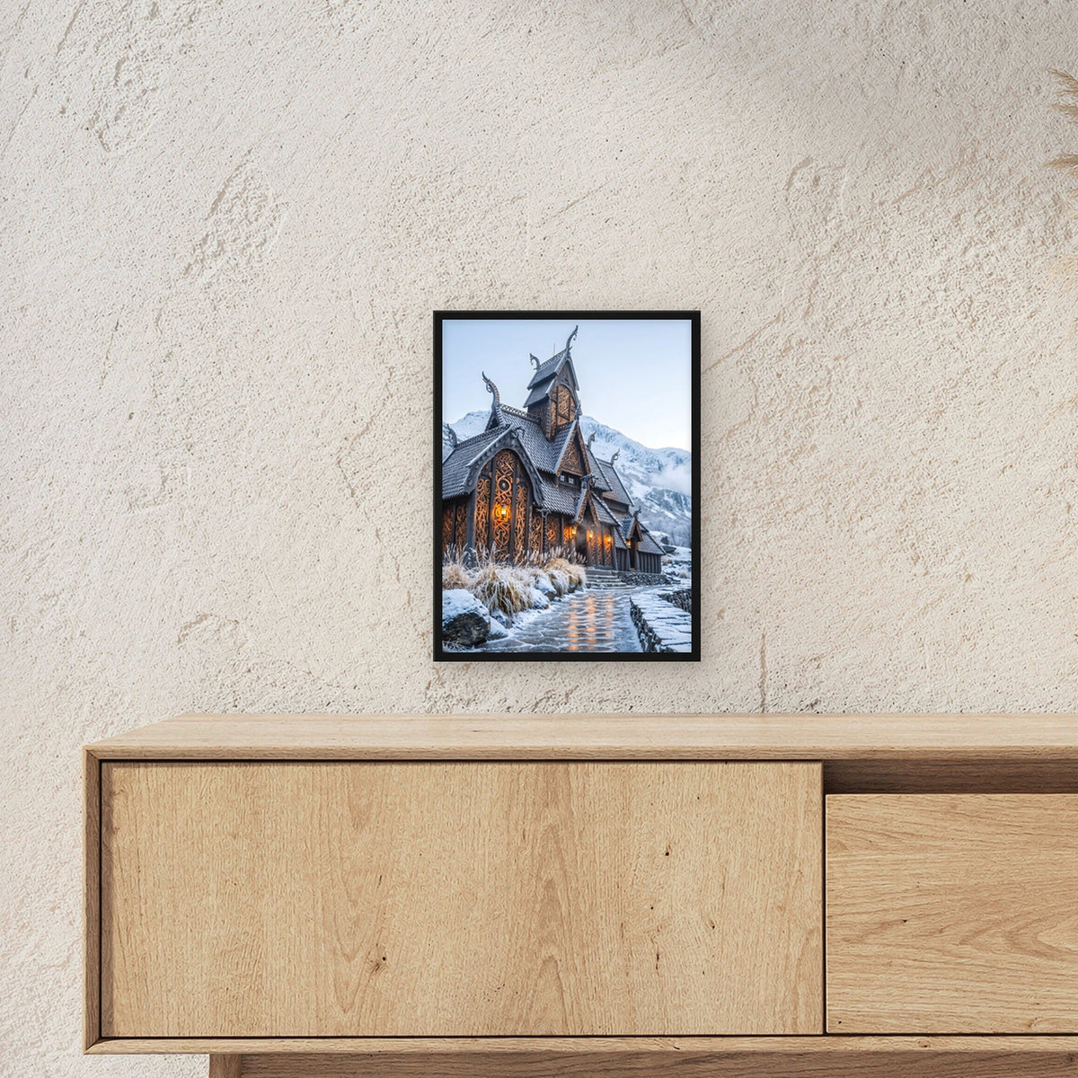 Stabkirche im Schnee – Nordische Stabkirche mit Drachenköpfen vor verschneiten Bergen, im schwarzen Holzrahmen, über einem Sideboard, zeigt die Größe im Raum