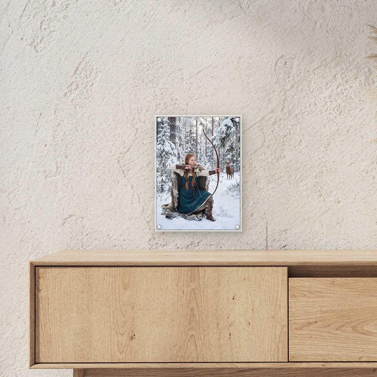 Die Winterjägerin – Rothaarige Bogenschützin zielt im verschneiten Wald, auf Acrylglas mit Abstandshaltern, über einem Sideboard